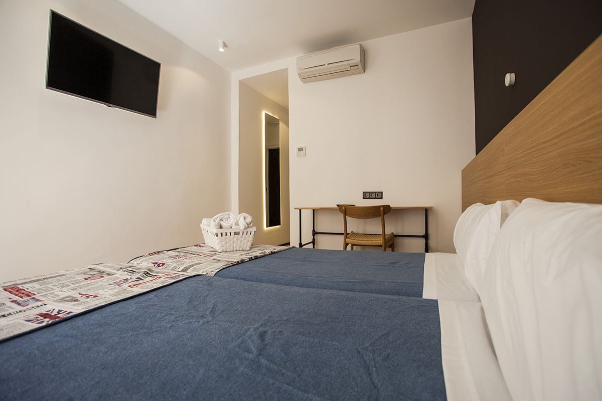 A hotel room with a bed, a desk, a chair, a TV, and an air conditioning unit.