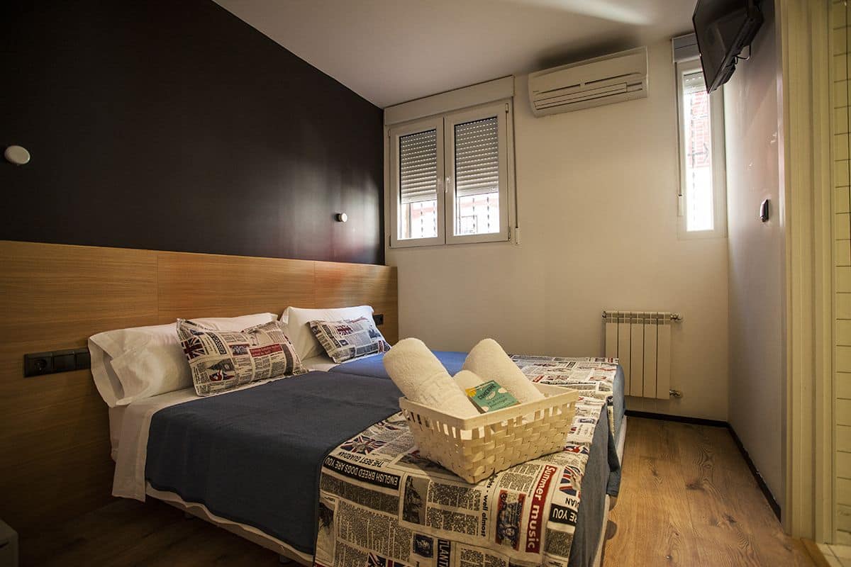Um quarto com cama, almofadas, um cesto de toalhas, janela com persianas e um radiador.