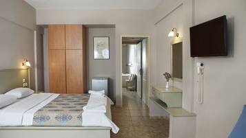 A hotel room with a bed, a wardrobe, a desk with a mirror, and a TV mounted on the wall.