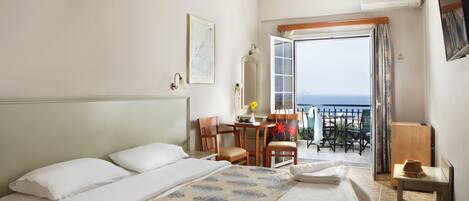 A hotel room with a large bed, a desk, and a view of the sea through an open door.