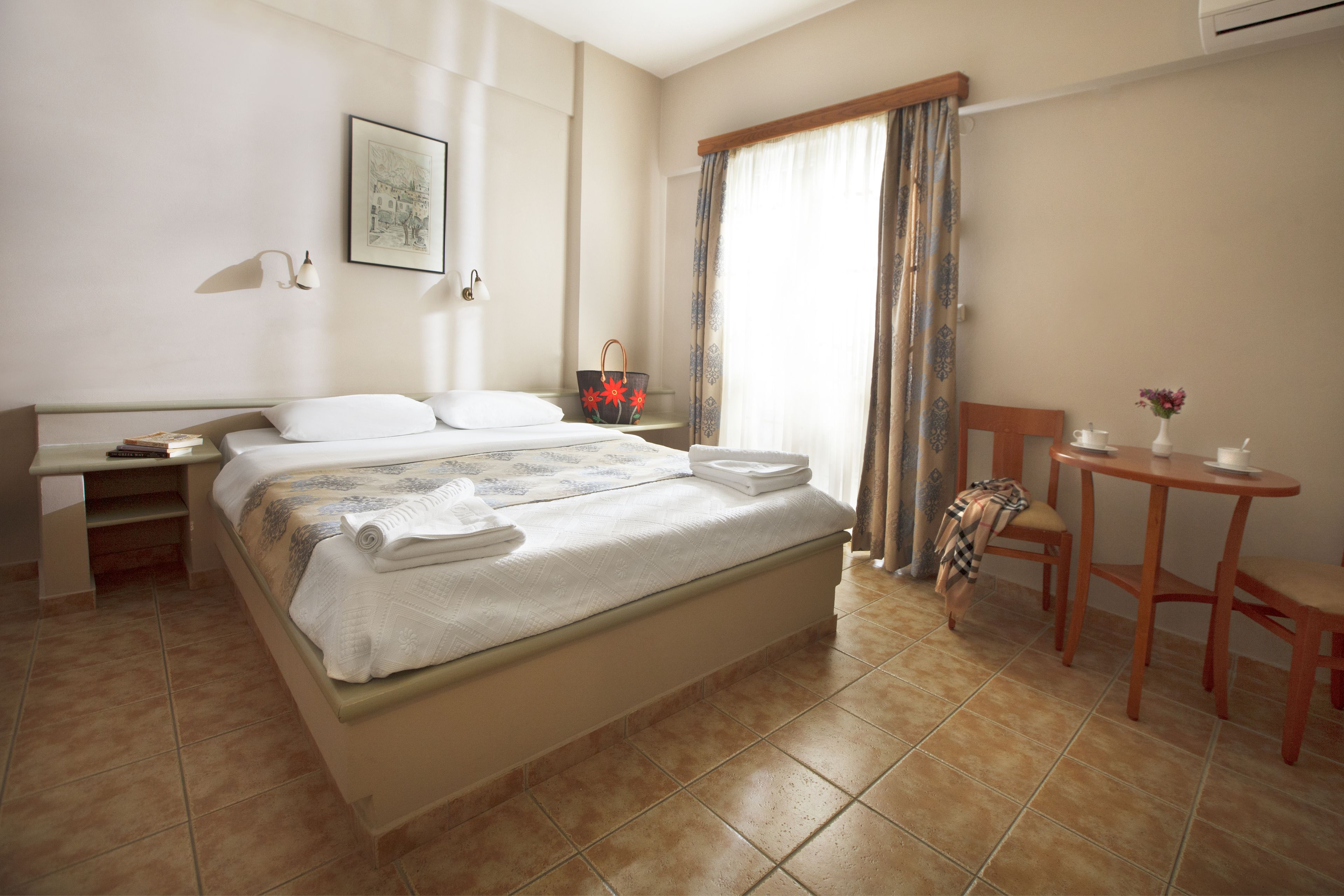 A hotel room with a bed, bedside table, and a small table with a chair.