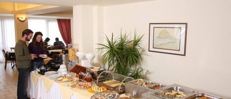 Un'area buffet con diversi cibi e una pianta grande sullo sfondo.