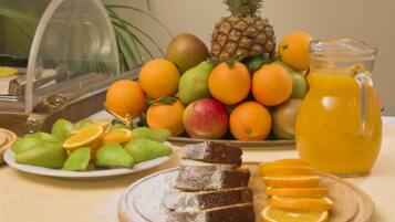 Un bufé de desayuno con frutas, una piña, naranjas, una jarra de jugo de naranja y un plato de pasteles.