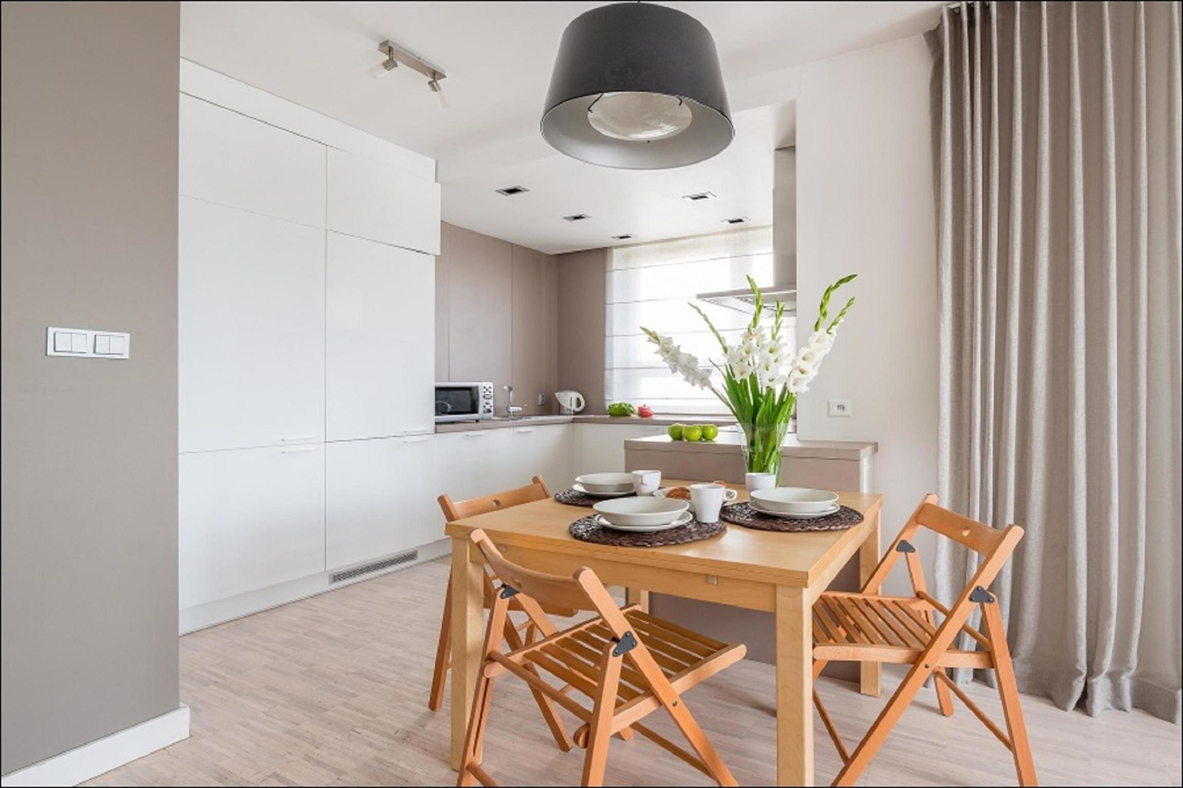 A modern kitchen with white cabinets, a wooden dining table with four chairs, and a pendant light above.