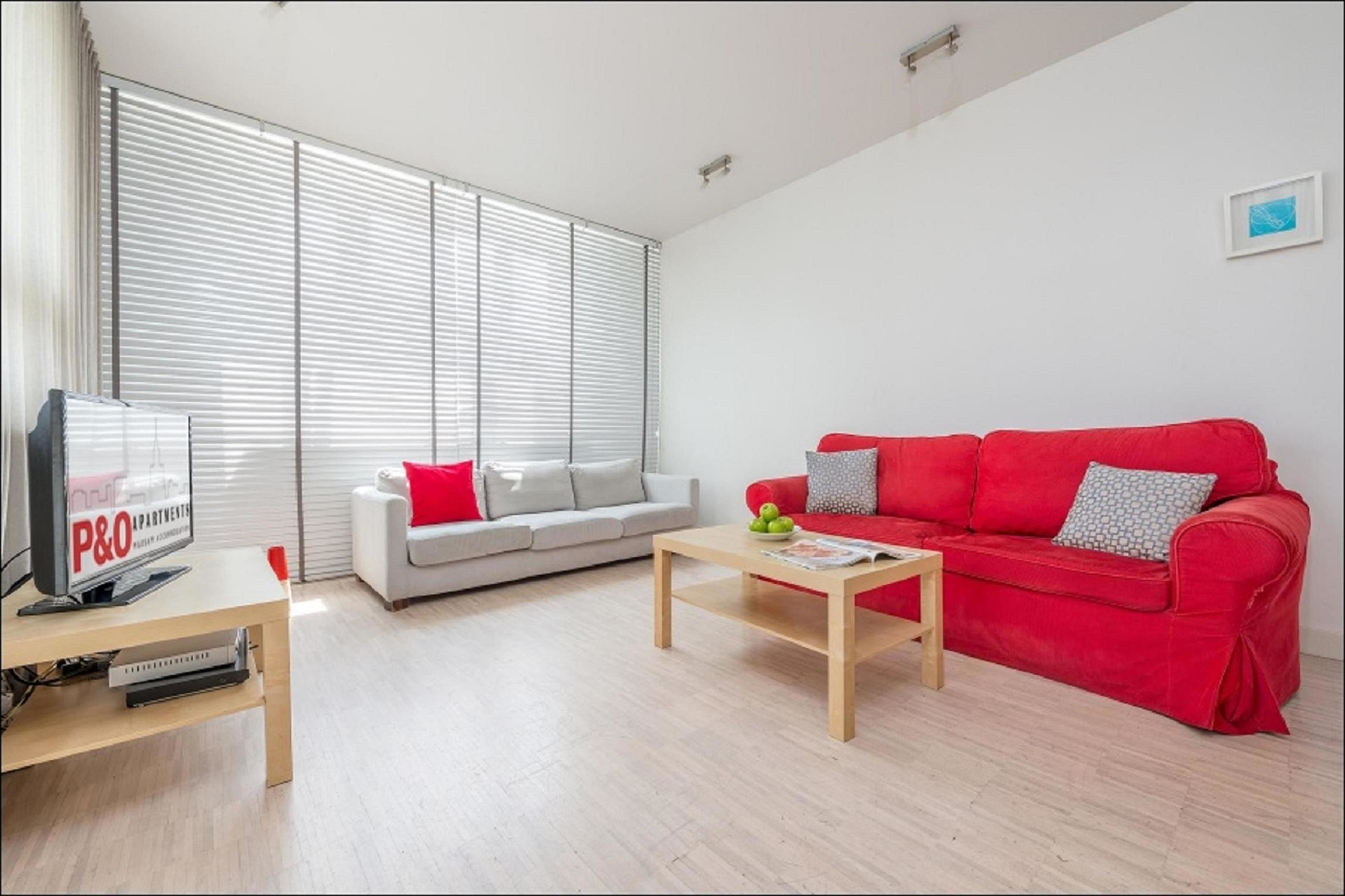 Una sala moderna con un sofá rojo, un sofá blanco, una mesa de centro de madera y un televisor sobre un mueble bajo.