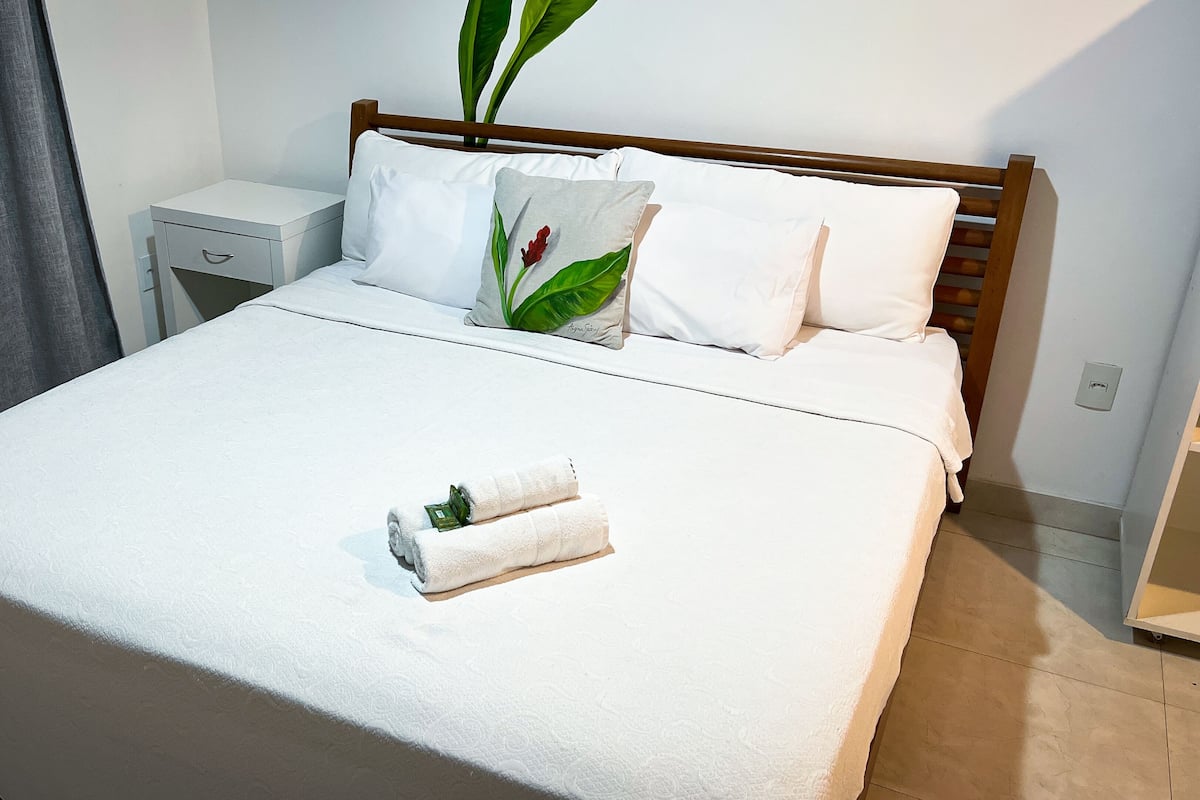 A neatly made bed with white linens, a small bedside table, and a potted plant.