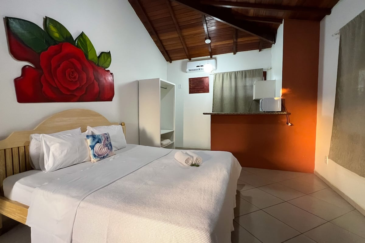A hotel room with a bed, a nightstand, a wall-mounted air conditioning unit, a mirror, and a towel on the bed.