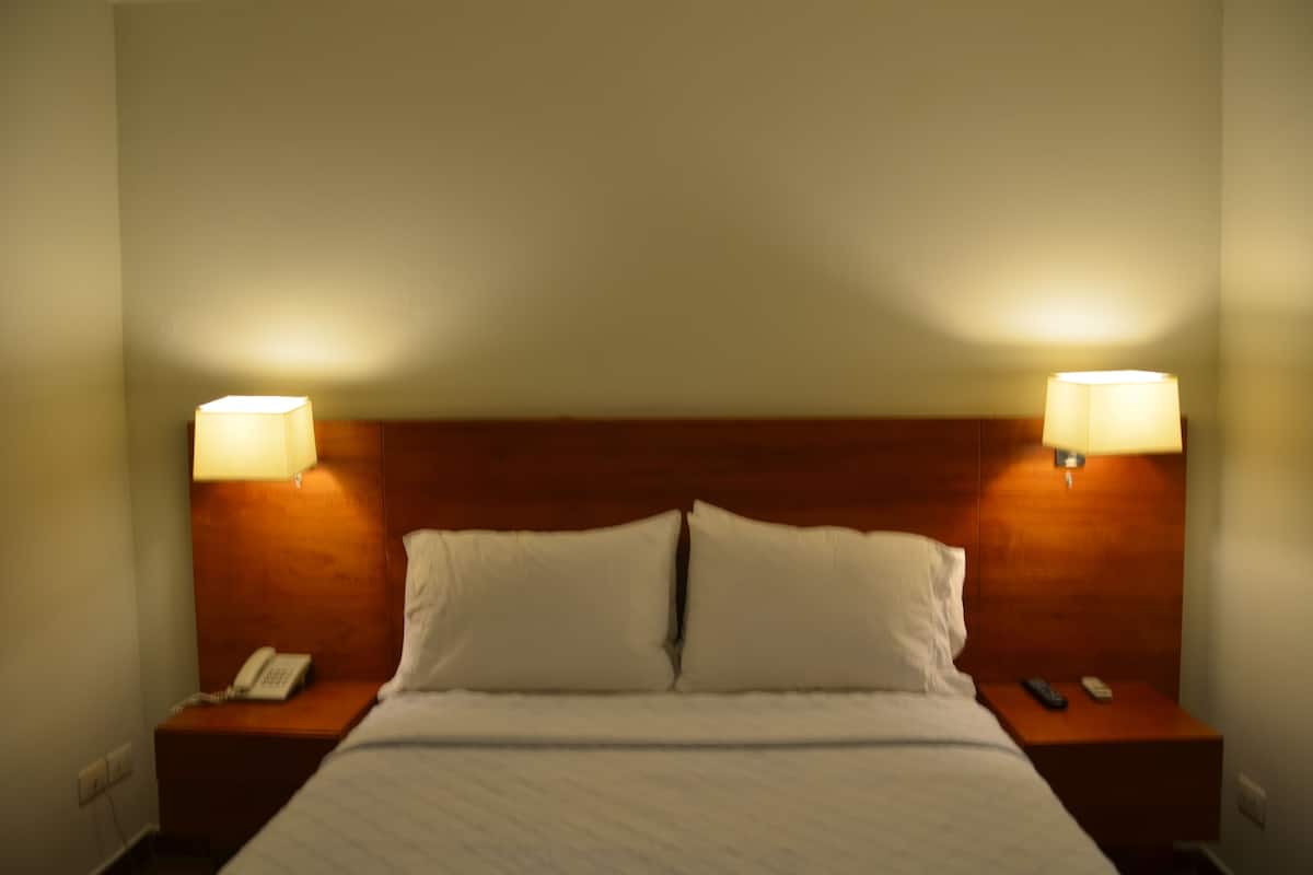 A hotel room with a wooden headboard, two bedside lamps, a telephone, and a bed with white linens.