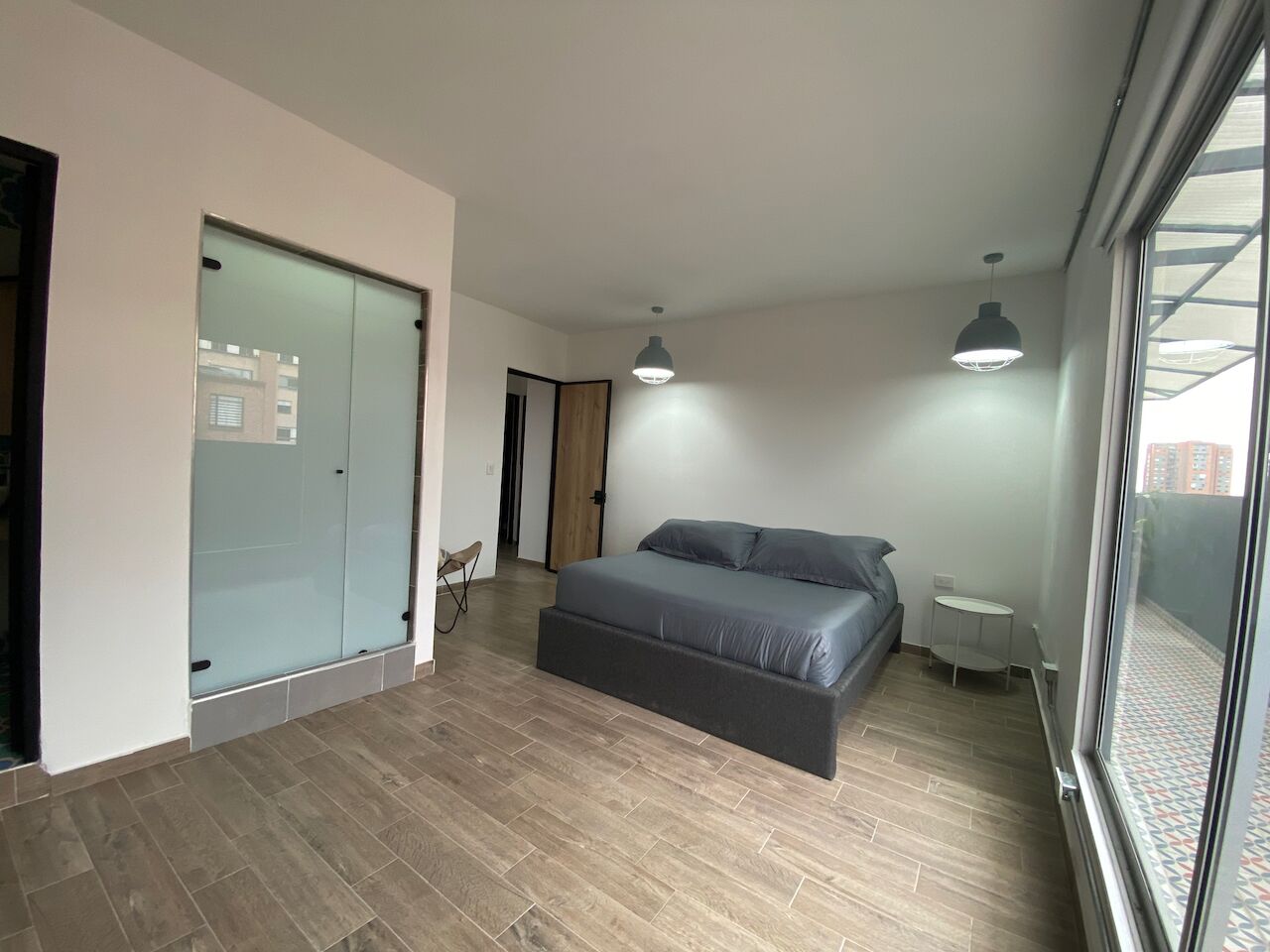 Un dormitorio moderno con una cama grande, un ventanal corredero y una mesita junto a la ventana.