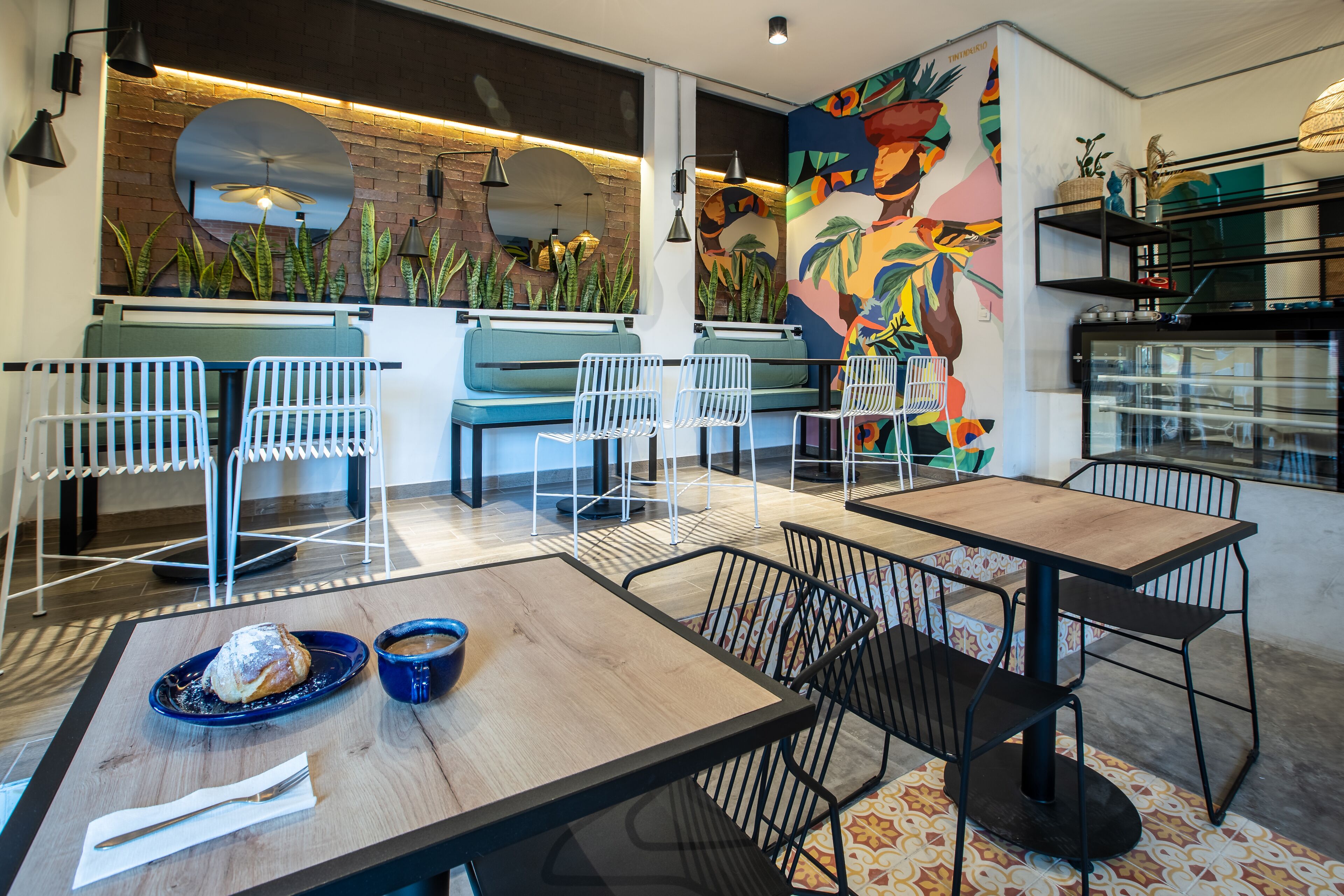 A modern cafe with wooden tables and chairs, a mural, and plants.