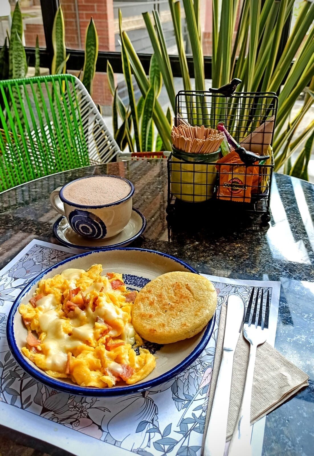 A breakfast setting with scrambled eggs, a biscuit, and a cup of coffee on a table with a placemat.