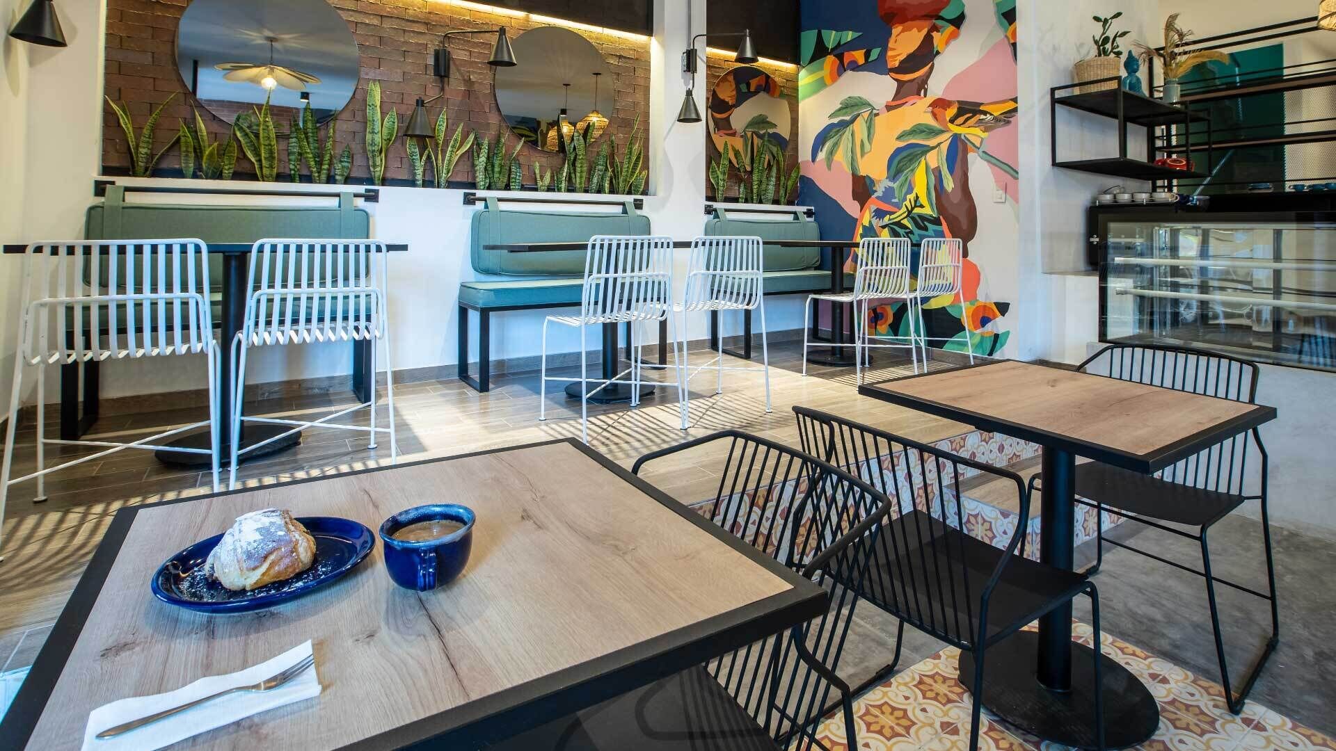 Un interior de restaurante con disposición de mesas, un mural y una barra con vitrina.