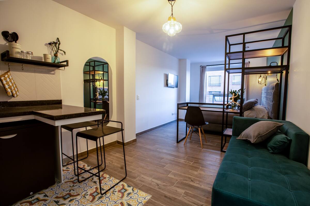 Uma sala de estar moderna com um sofá verde, uma cozinha com um banco de bar e uma mesa de jantar com cadeiras.