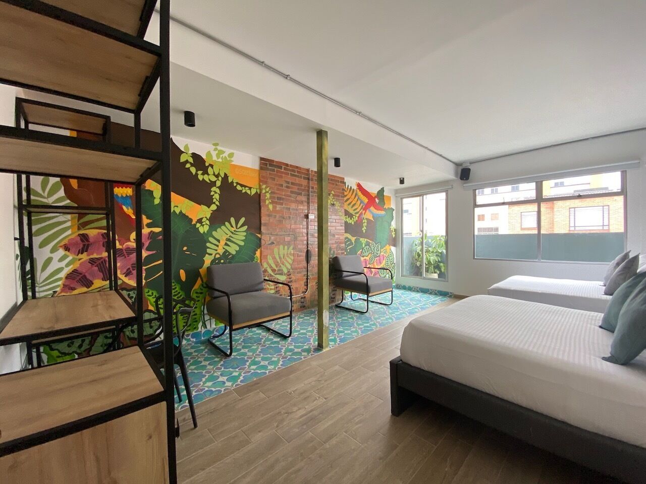 A modern hotel room with a large bed, two chairs, a small table, and a colorful mural on the wall.