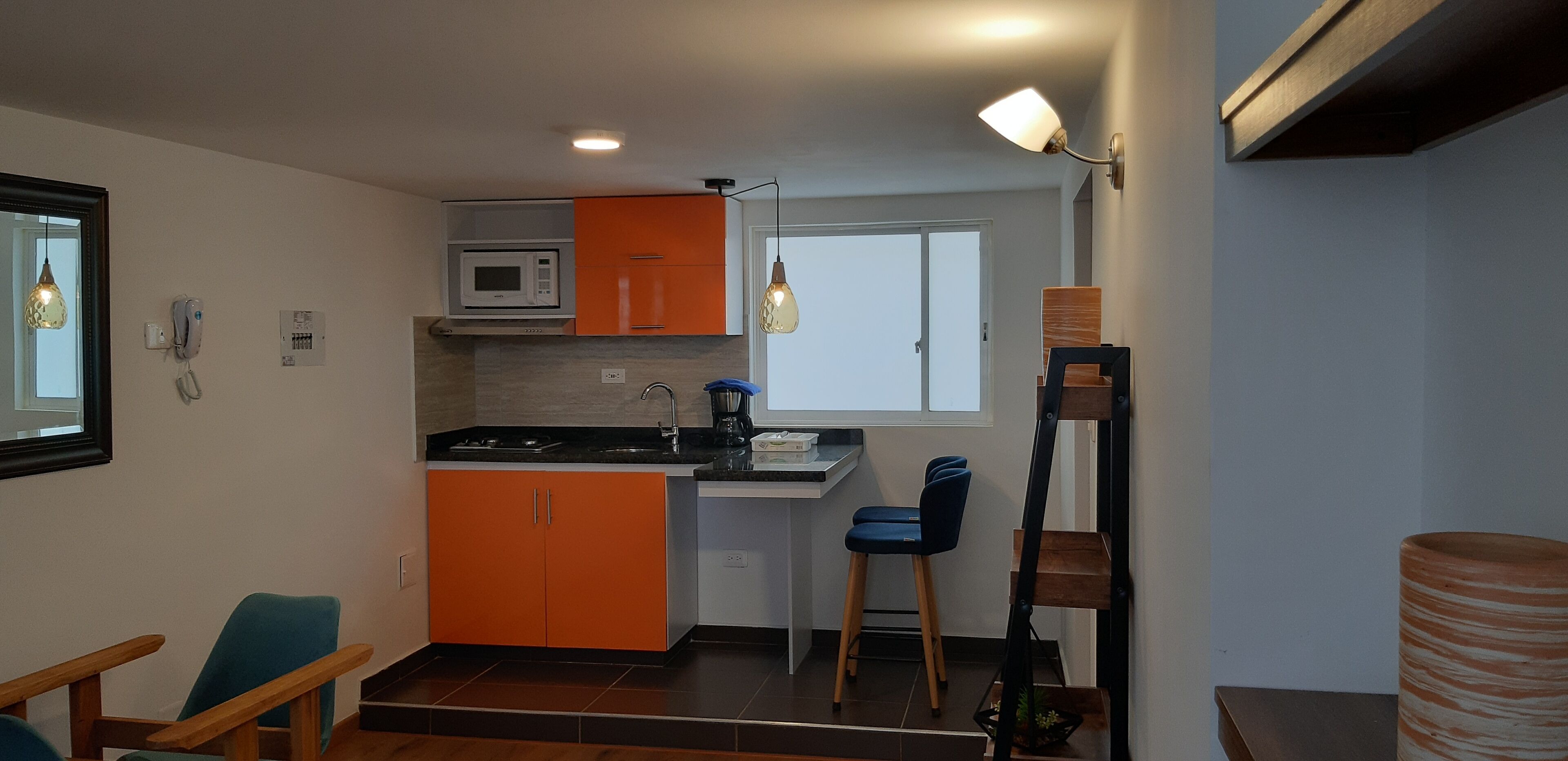 Een compacte keuken met oranje kastjes, een magnetron en een klein eethoekje met blauwe stoelen.