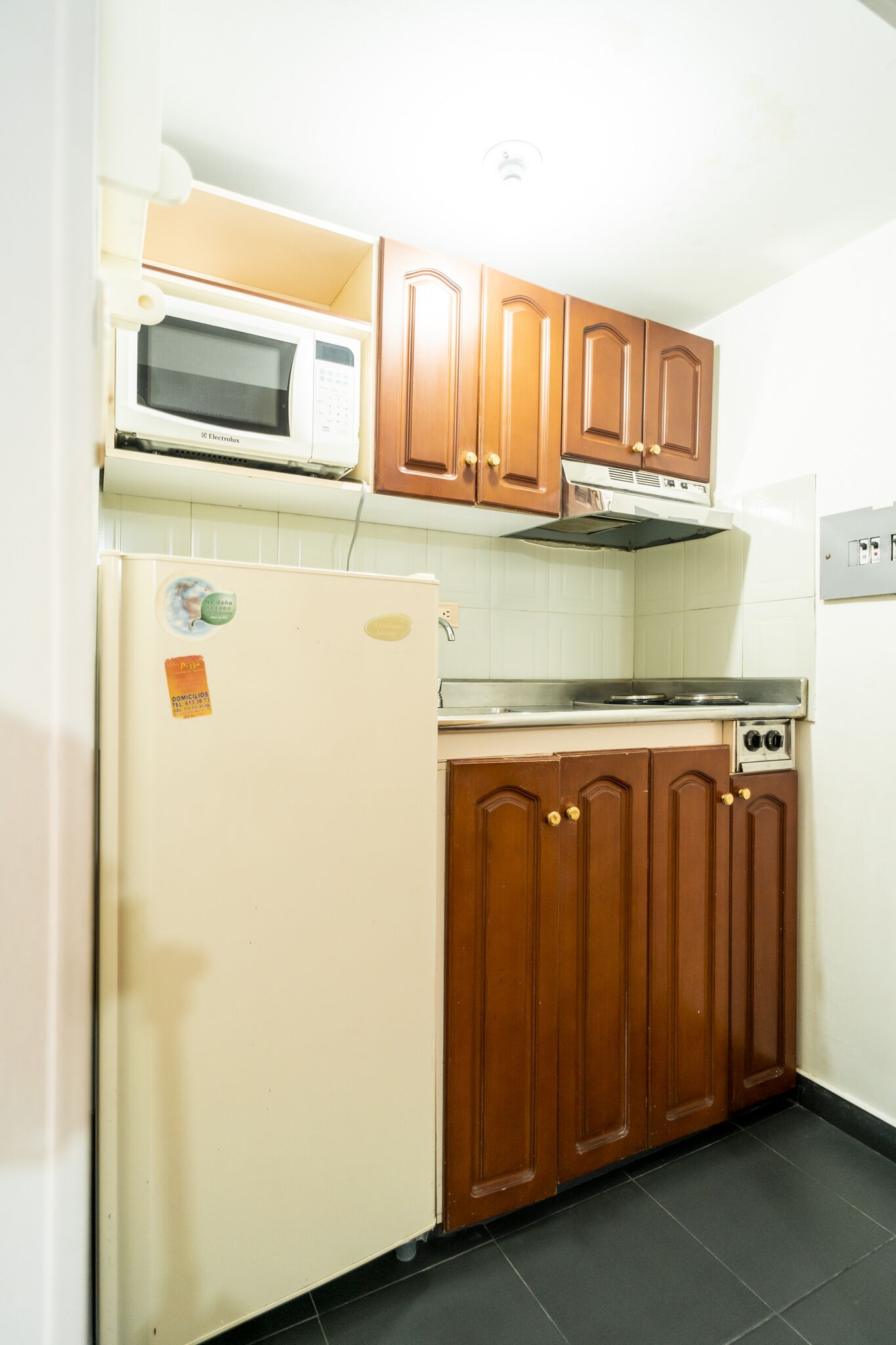 A compact kitchen with a white refrigerator, a microwave, wooden cabinets, and a stove.