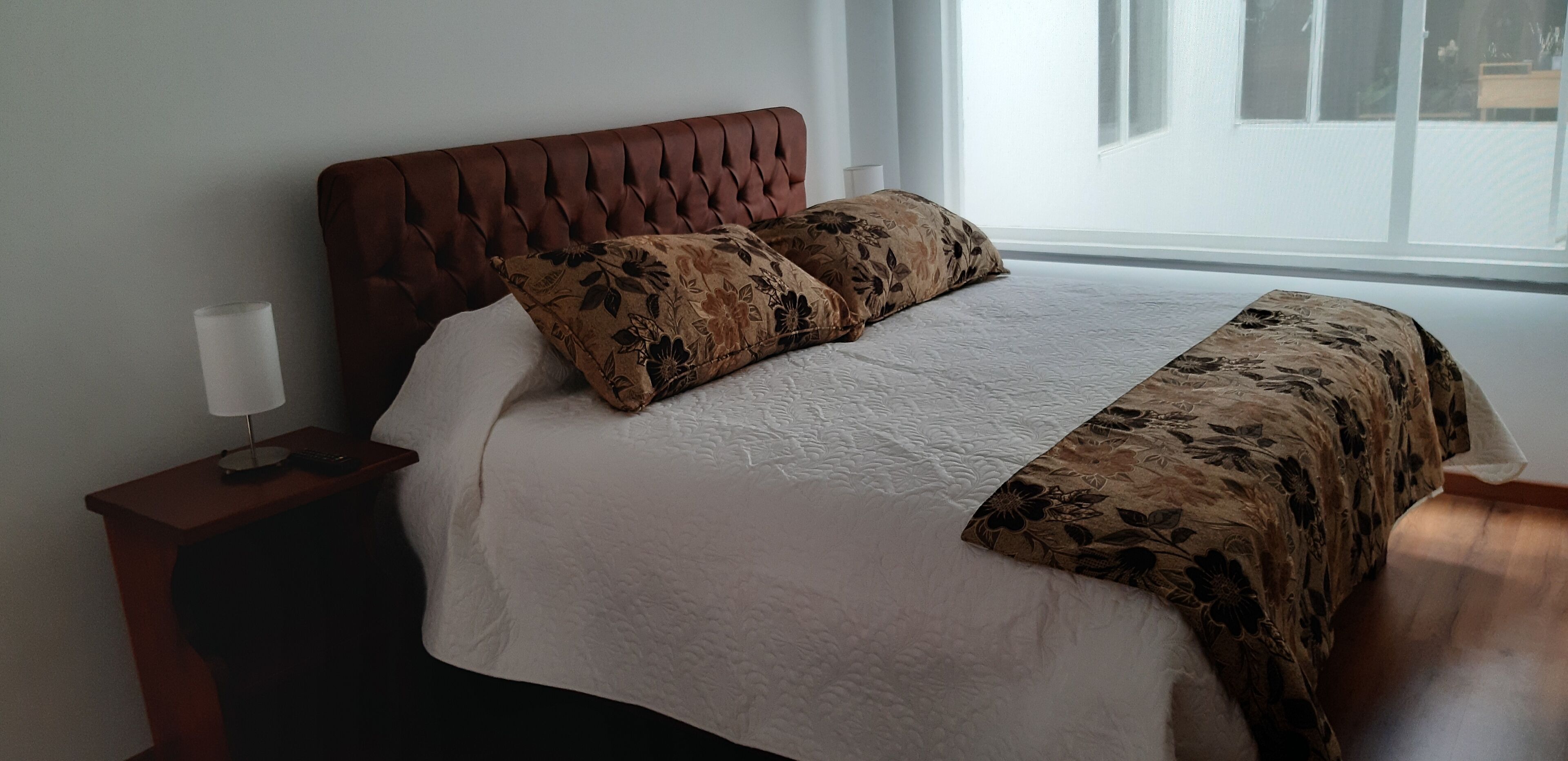 A bedroom with a tufted headboard, a floral-patterned bedspread, and a bedside table with a lamp.