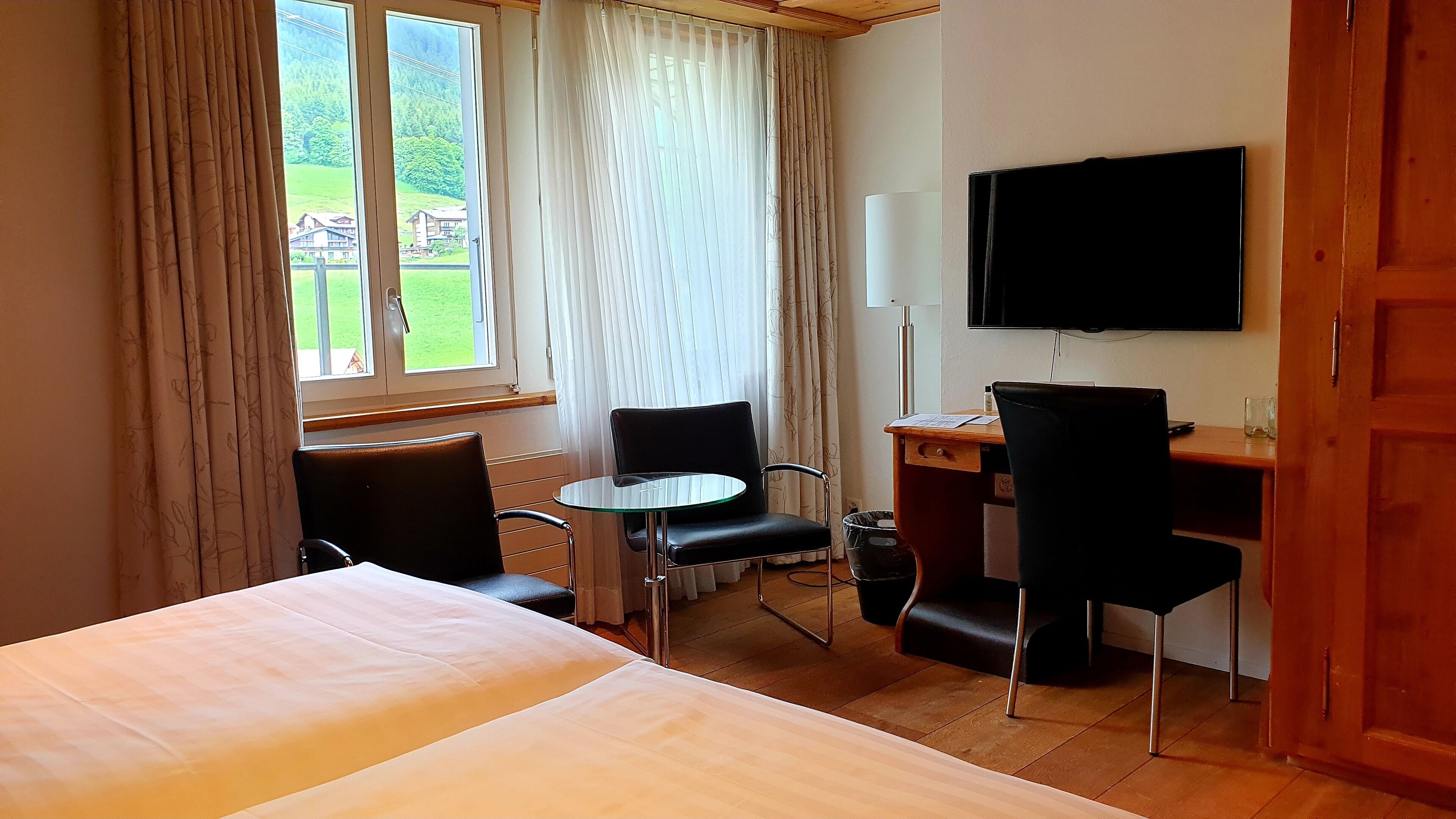 Una habitación de hotel con cama, escritorio, silla, televisor y ventana con cortinas.