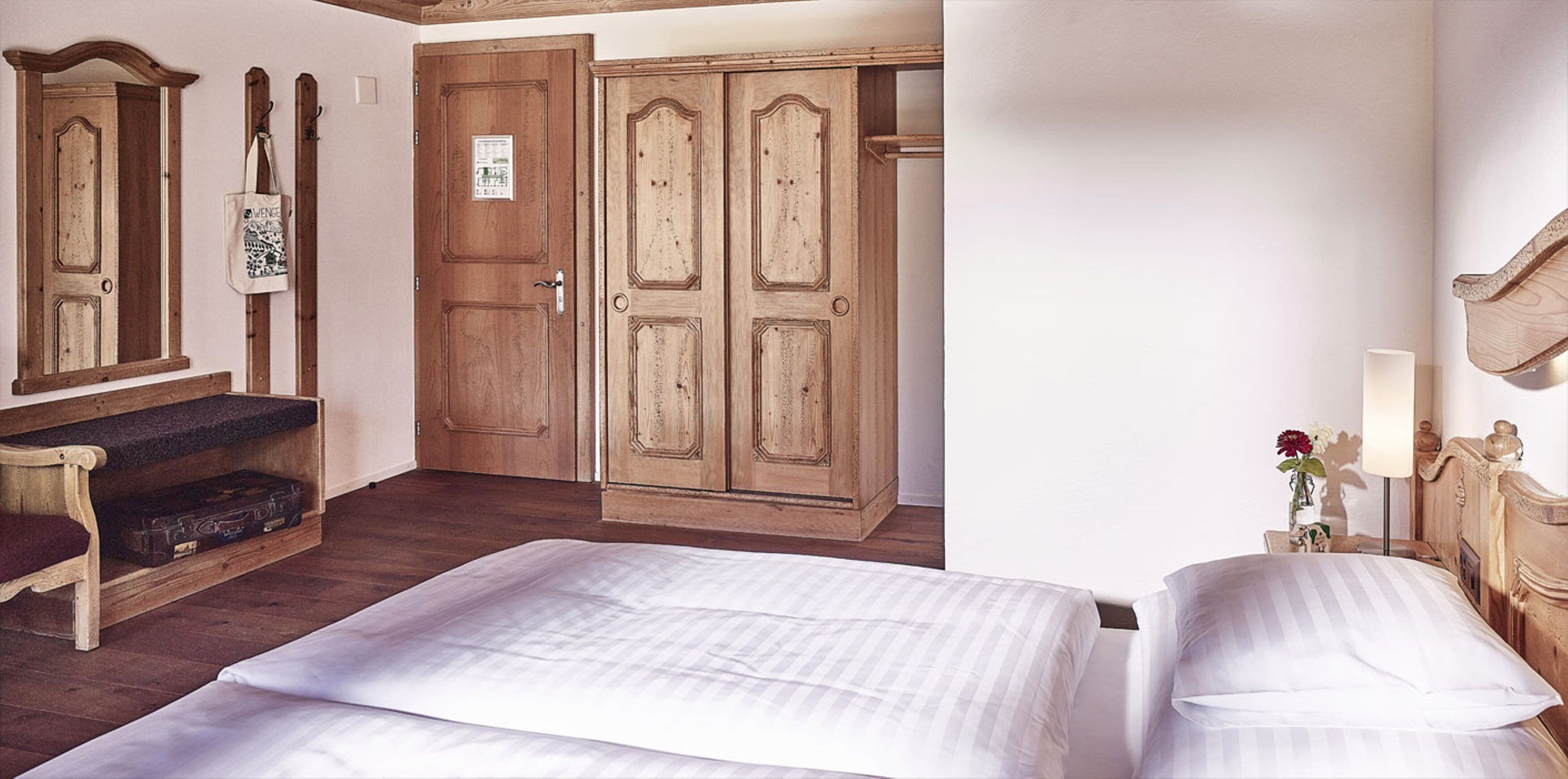 A room with a bed, wooden wardrobe, and a bench with a suitcase.