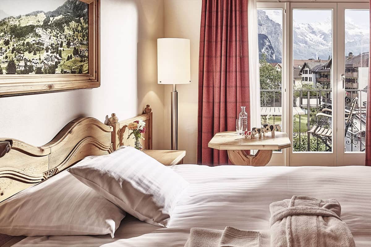 Een hotelkamer met een bed, een stoel, een tafel met lamp en een raam met gordijnen.