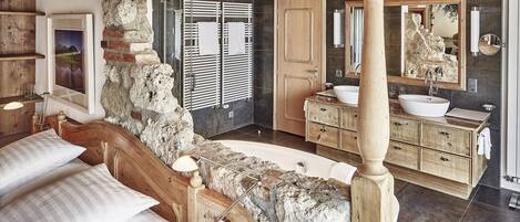 Un baño con pared de piedra, armarios de madera, un espejo grande y una bañera.