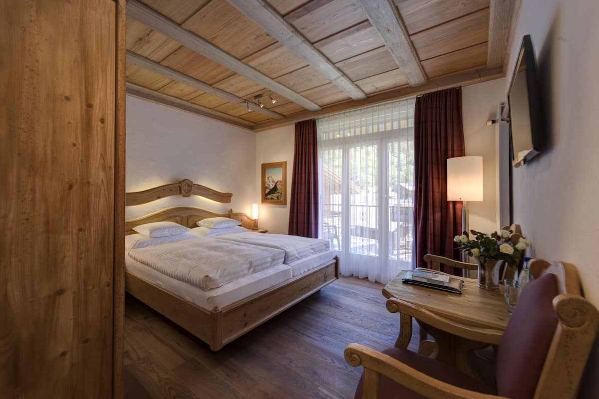 Een kamer met houten frame, een bed, een tafel met stoelen en een raam met gordijnen.