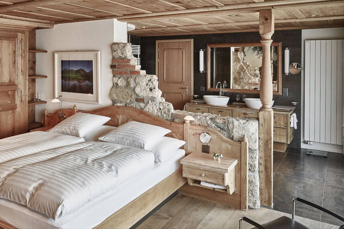Een slaapkamer met een groot bed, een houten garderobe en een badkamer met een stenen muur en houten accessoires.