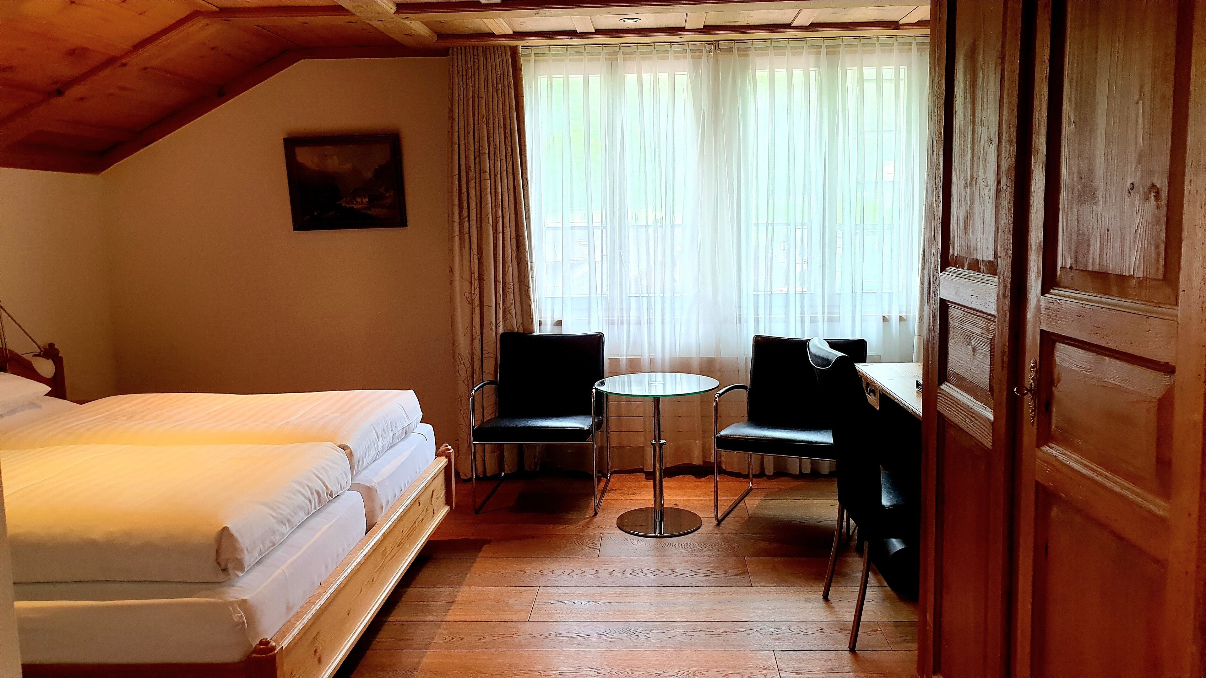 A room with a bed, two chairs, a small table, and a window with curtains.