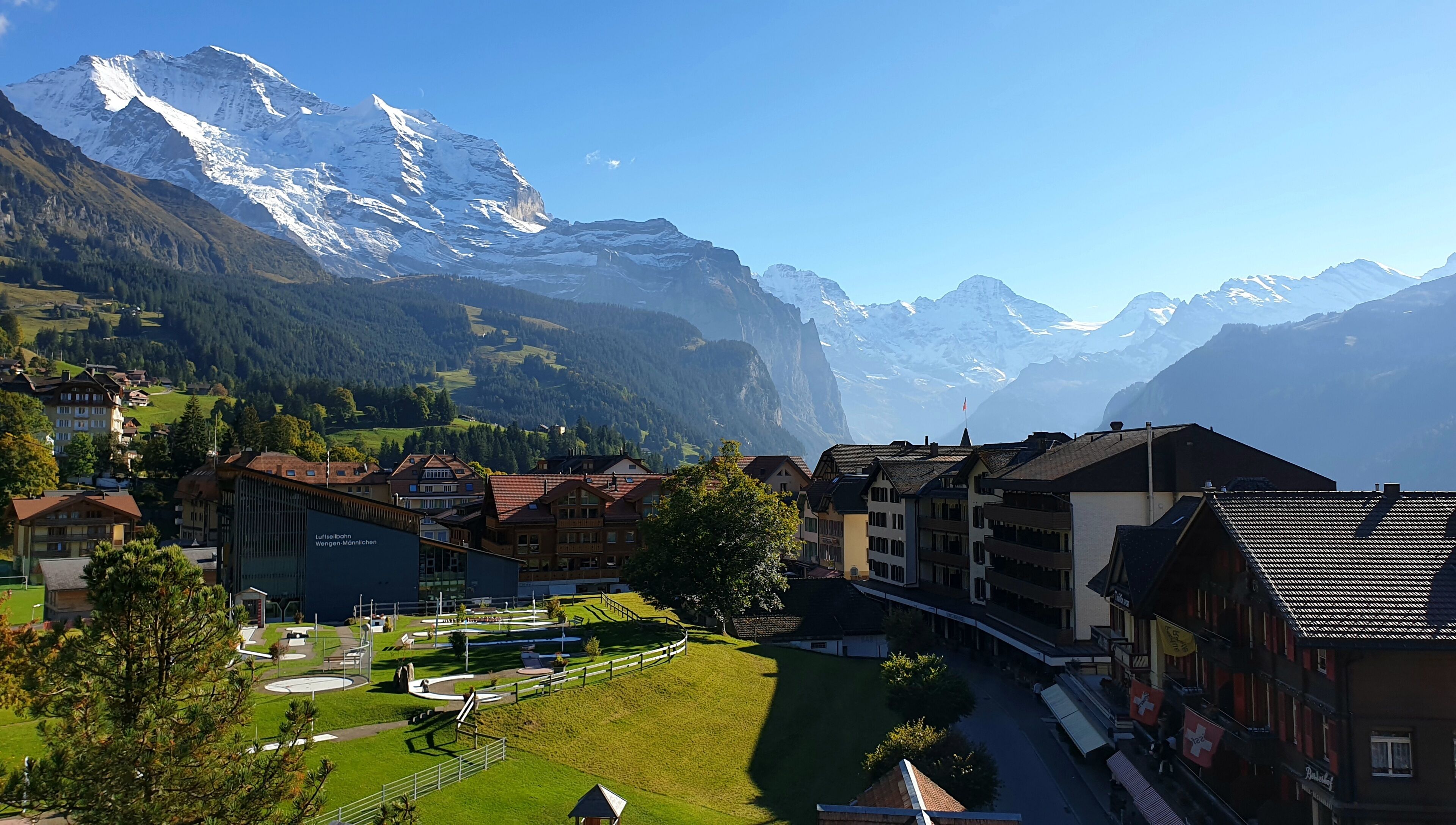 Une ville à l’architecture traditionnelle, avec une place centrale et, en arrière-plan, des montagnes enneigées.
