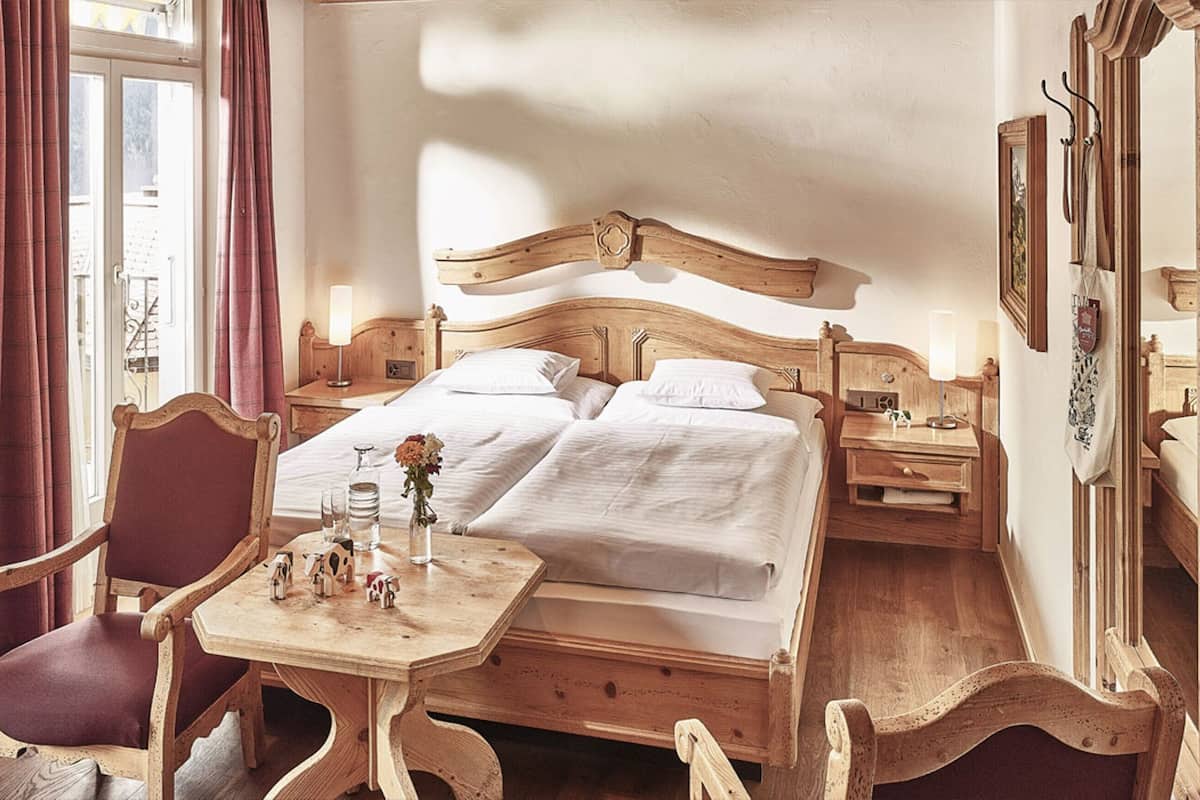 Een traditioneel houten bed met hoofdeinde, een tafeltje met een vaas en beeldjes, en een stoel.