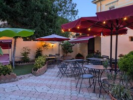 Un patio al aire libre con mesas y sillas, rodeado de plantas en macetas y árboles.