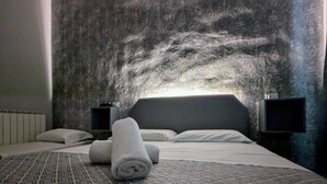 A hotel room with a patterned carpet, a neatly made bed with rolled towels, and a textured wall.