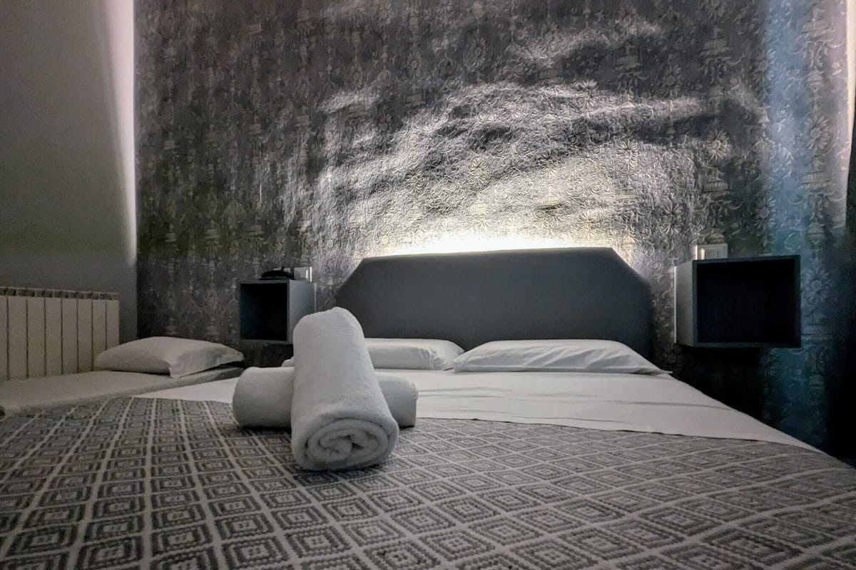 Ein Hotelzimmer mit einem gemusterten Teppich, einem ordentlich bezogenen Bett und flauschigen Handtüchern sowie einer strukturierten Wand.