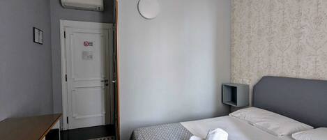 A hotel room with a bed, a desk, a chair, a patterned wall, and a door with a no smoking sign.