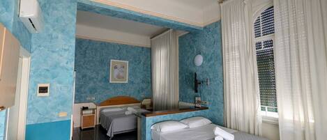 A hotel room with two beds, a desk, a chair, a window with curtains, and a wall-mounted air conditioner.