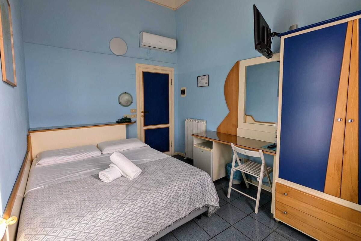 Ein Schlafzimmer mit Bett, Schreibtisch, Stuhl, Kleiderschrank und Klimaanlage.