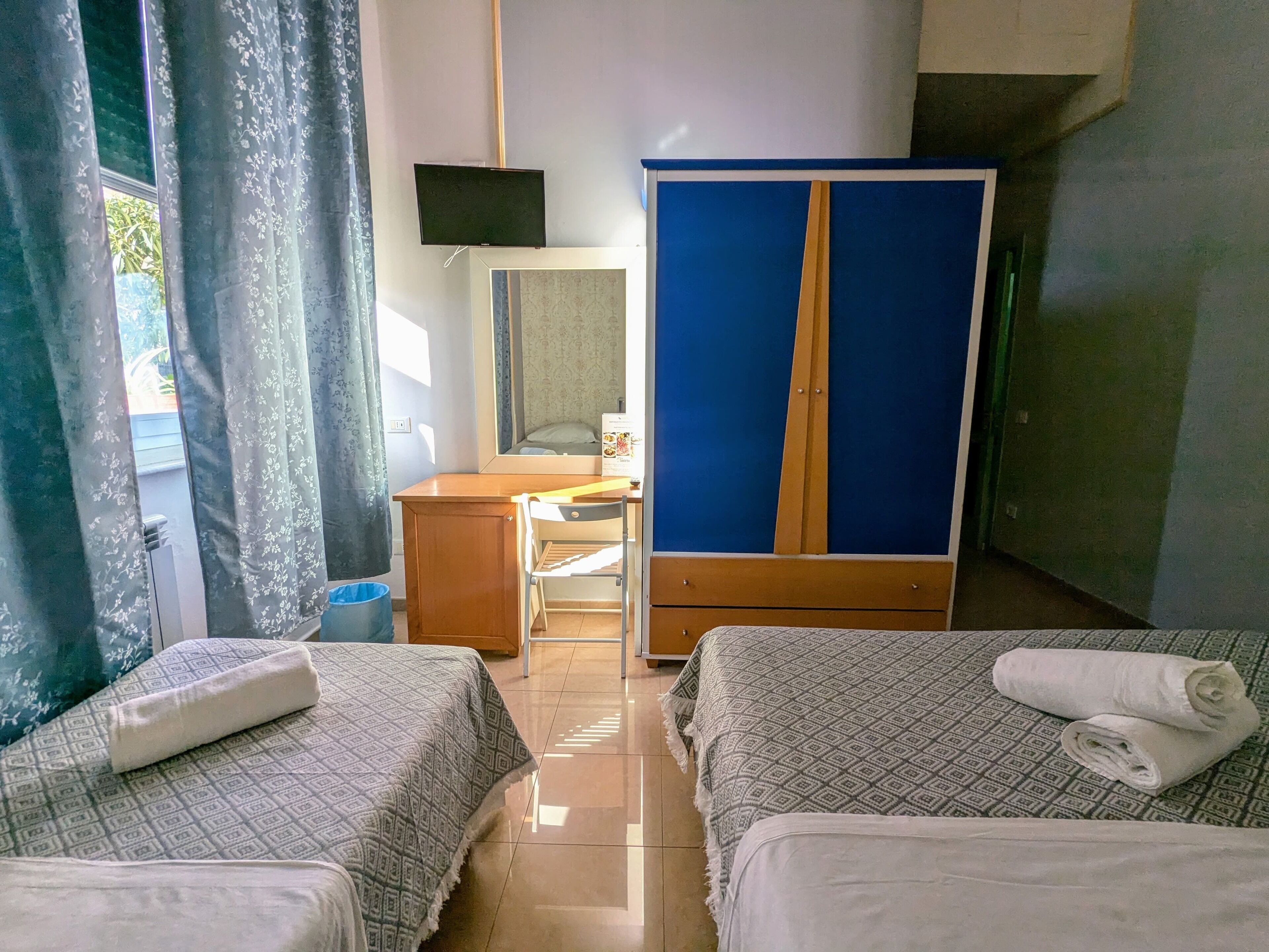 Una camera d'albergo con due letti, una scrivania, un armadio e una televisione.