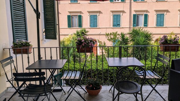 A balcony with two tables and chairs, potted plants, and a red umbrella.
