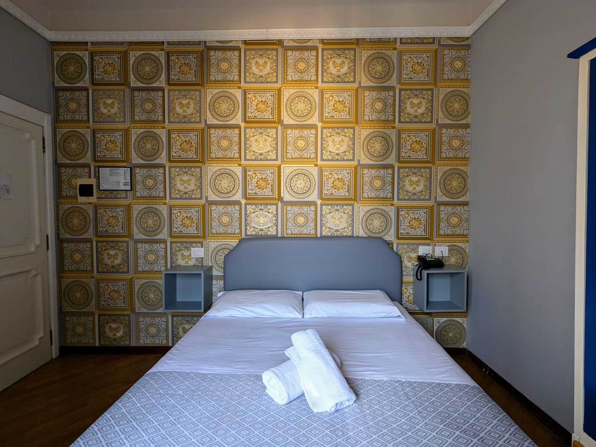 Habitación de hotel con una cama grande, dos mesitas de noche y un papel tapiz estampado.