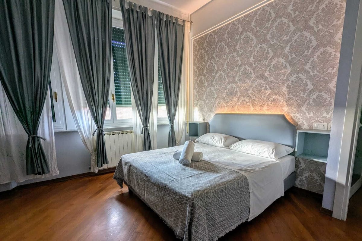 Ein Schlafzimmer mit Bett, Vorhängen, einer Wand mit Muster und einem Nachttisch.
