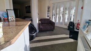 A kitchen with a granite countertop, a brown leather chair, and a white door with sheer curtains. - The Fawley (Shanklin)