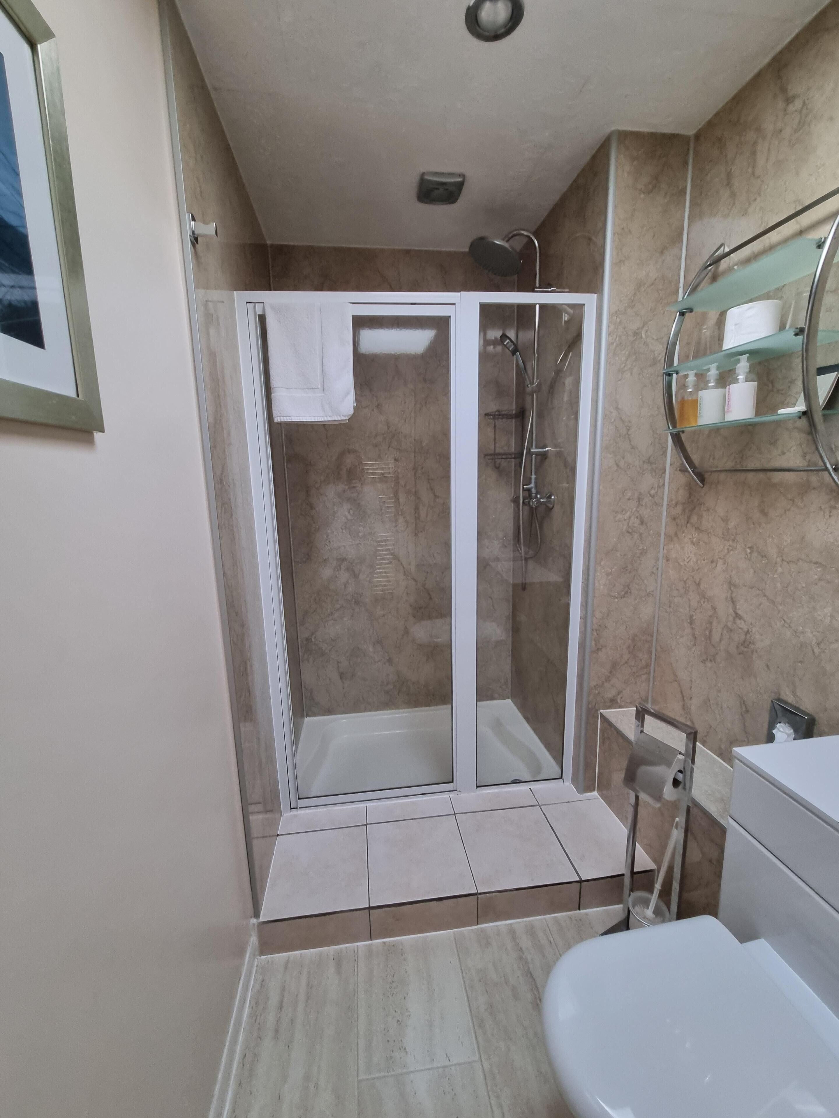 Une salle de bain moderne avec une douche à parois de verre, des toilettes blanches et une étagère en verre où sont rangés les articles de toilette.