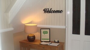 A wooden console table with a lamp, a framed welcome sign, and a framed 'How was your visit?' card. - The Fawley (Shanklin)