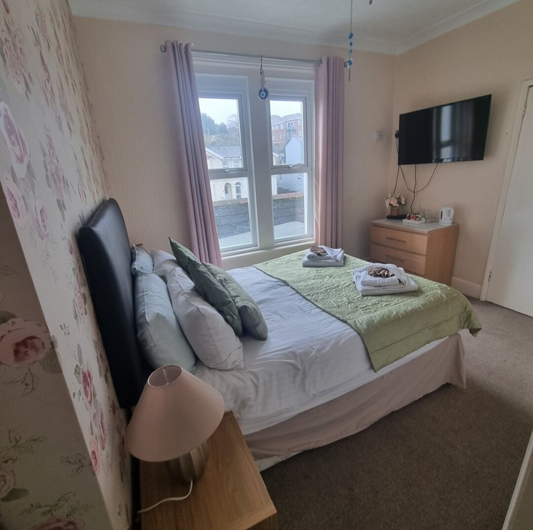 A bedroom with a bed, a bedside table, a lamp, a TV, and a window with curtains.