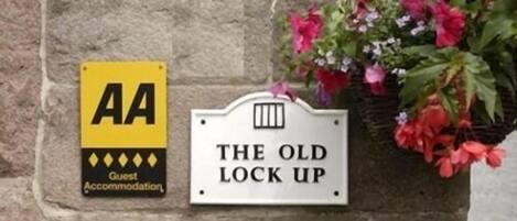 Egy tábla, amelyen a „The Old Lock Up” felirat szerepel, és egy sárga színű „AA Guest Accommodation” tábla.