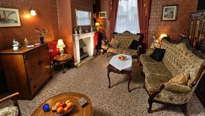 Una sala de estar tradicional con chimenea, papel tapiz estampado y muebles clásicos.