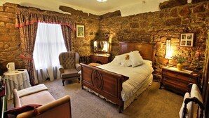 Un dormitorio con pared de piedra, una cama de madera, una silla, una mesita de noche y una lámpara.