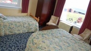 Camera d'albergo con due letti, una finestra con tende, una sedia e vista sull'esterno.