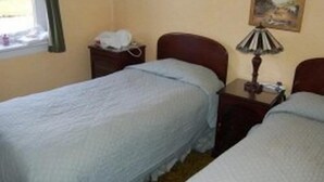 Una stanza con due letti singoli, un comodino con una lampada, un altro comodino con il telefono e una finestra che si affaccia sull'esterno.