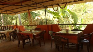 An outdoor patio with tables and chairs, surrounded by lush greenery and banana plants. - Yellow House (Vagator)